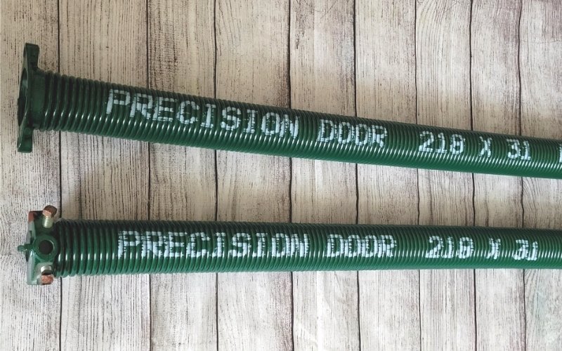 Lengthwise photo of two green garage door springs that say "Precision Door"